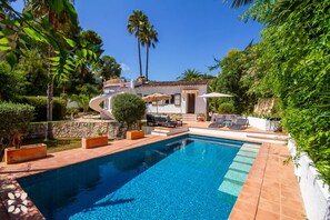 A swimming pool with a sun terrace, surrounded by lush greenery and palm trees.