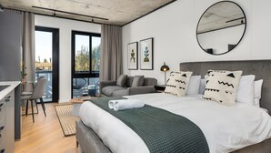 Une chambre d’hôtel moderne avec un grand lit, un canapé gris et un coin repas.