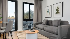 Un salon moderne avec un canapé gris, une table basse ronde et une vue sur l’extérieur grâce à une grande fenêtre.