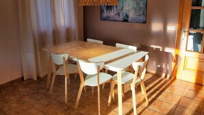 Un comedor con una mesa de madera y sillas blancas, una lámpara colgante y un cuadro en la pared.