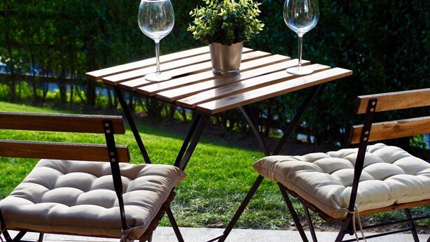 Un área de estar al aire libre con dos sillones acolchados y una mesita pequeña, cada uno con una copa de vino.