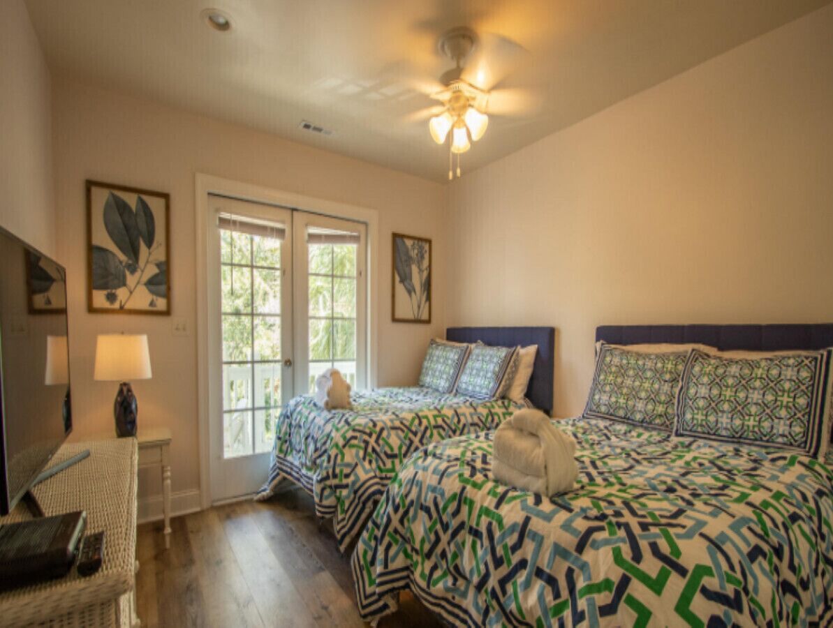 A bedroom with two beds, a ceiling fan, and a window with blinds.