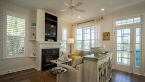 A spacious living room with a fireplace, a ceiling fan, and large windows. - 87 Ocean Creek - Canal w/Shared Dock (Fripp Island)