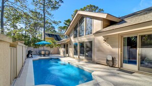 A modern house with a swimming pool, large windows, and a covered patio area. - 3rd Row Ocean - Dog Friendly Sea Pines Home w/ FREE Pool Heat Seasonally! (Hilton Head Island)