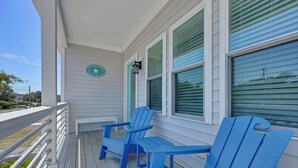 Eine Veranda mit zwei blauen Adirondack-Stühlen, einem weißen Geländer und einem Schild mit der Aufschrift 'Pier Review'.