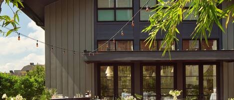 A building with large windows and a brick patio area with round tables set up for an event.