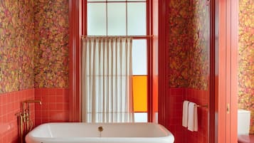 A bathroom with a freestanding bathtub, a wooden stool with toiletries, and a unique yellow chandelier.