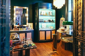 A boutique hotel interior with a wooden floor, a mirror with a gold frame, a display cabinet with various items, and a green suitcase on a table.