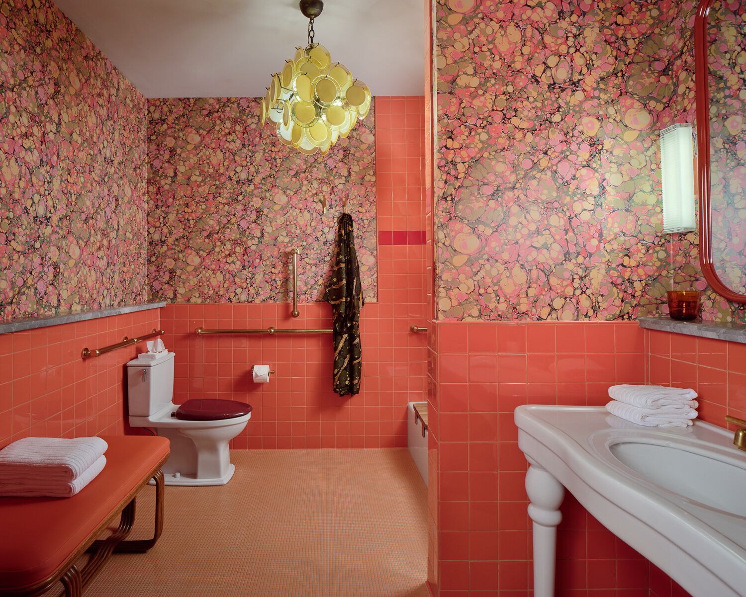 Ein Badezimmer mit blumigem Wandpapier, einem weißen Waschbecken, einer Toilette und einer Sitzbank mit Handtüchern.