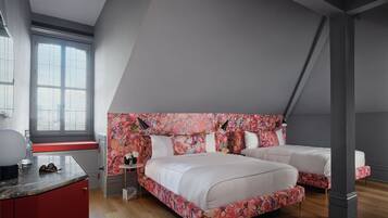 Ein Schlafzimmer mit schrägen Wänden, einem großen Bett mit einem blumengemusterten Kopfteil, einem Nachttisch und einem Fenster mit Jalousien.