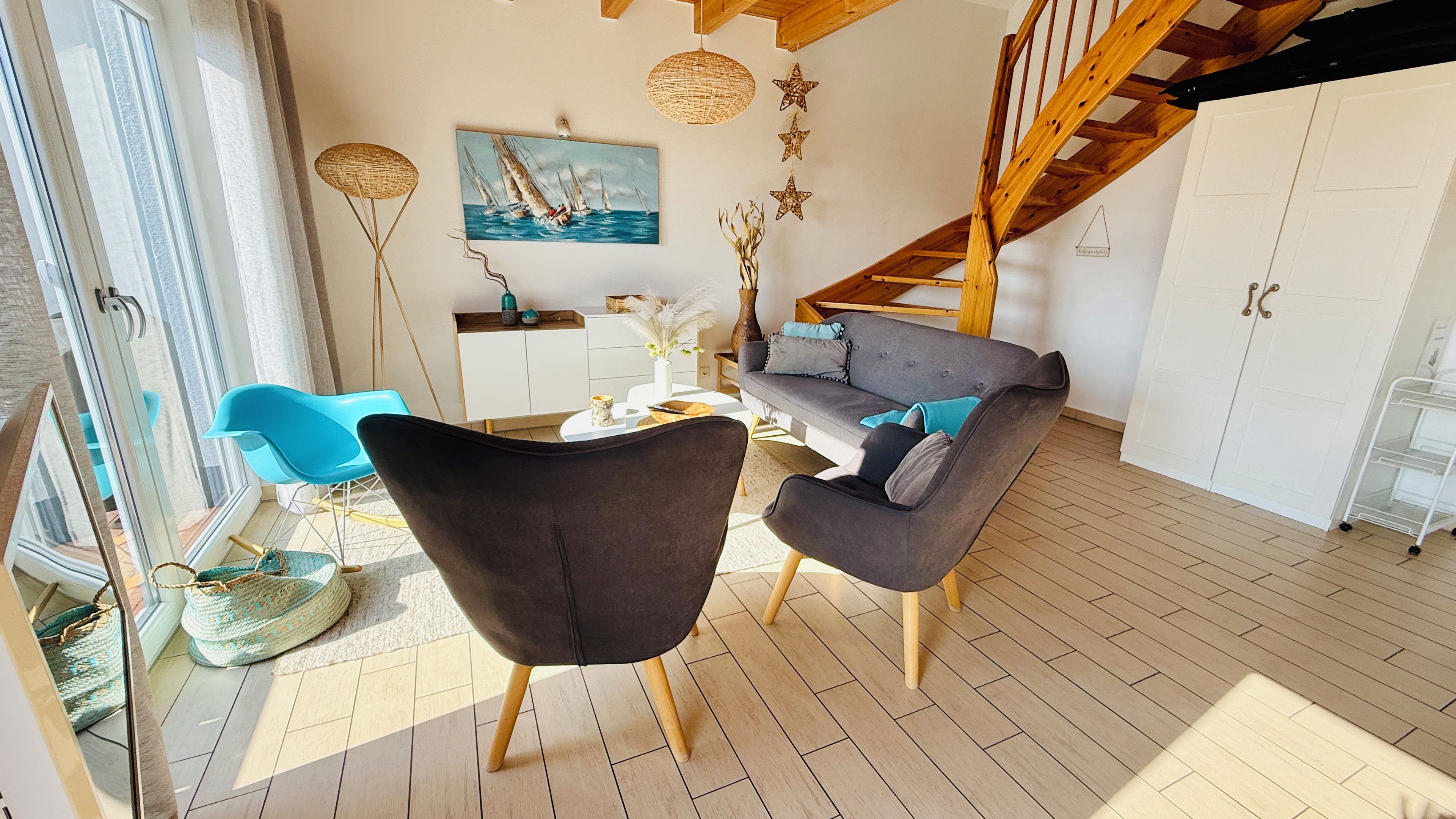 Un salon moderne avec un canapé, des fauteuils et un tableau représentant des voiliers.
