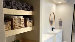 A modern bathroom with wooden shelves holding towels, a sink, and a mirror. - Great Vacation Home, Swim up Bar, Outdoor Living, New Pickleball Court (Phoenix)