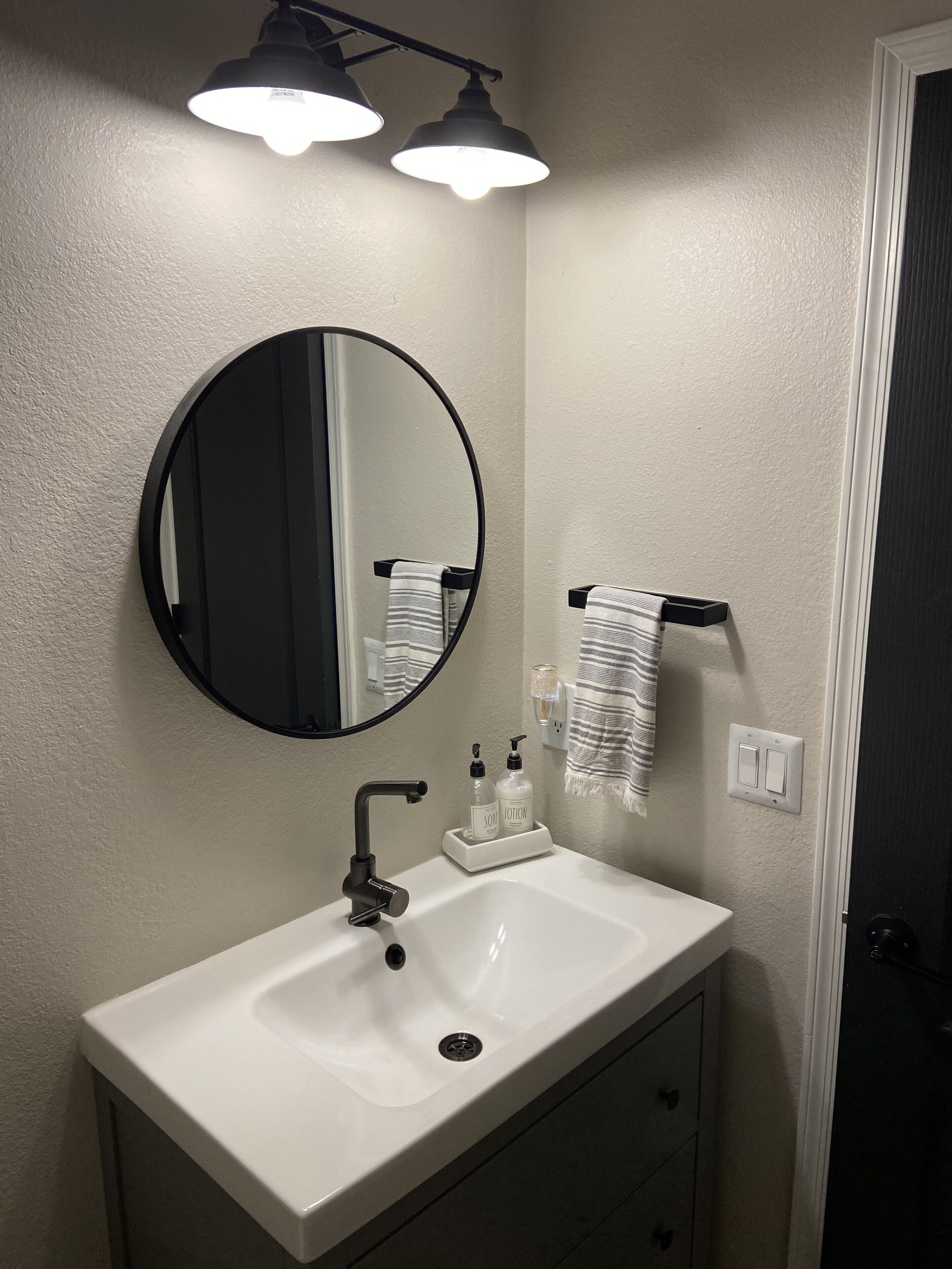A bathroom with a white sink, a round mirror, and two overhead lights.