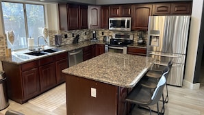 A modern kitchen with granite countertops, stainless steel appliances, and dark wood cabinetry. - Great Vacation Home, Swim up Bar, Outdoor Living, New Pickleball Court (Phoenix)