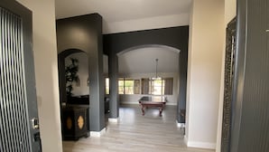 A spacious hallway with a pool table, a dark-toned reception desk, and a large window providing natural light. - Great Vacation Home, Swim up Bar, Outdoor Living, New Pickleball Court (Phoenix)