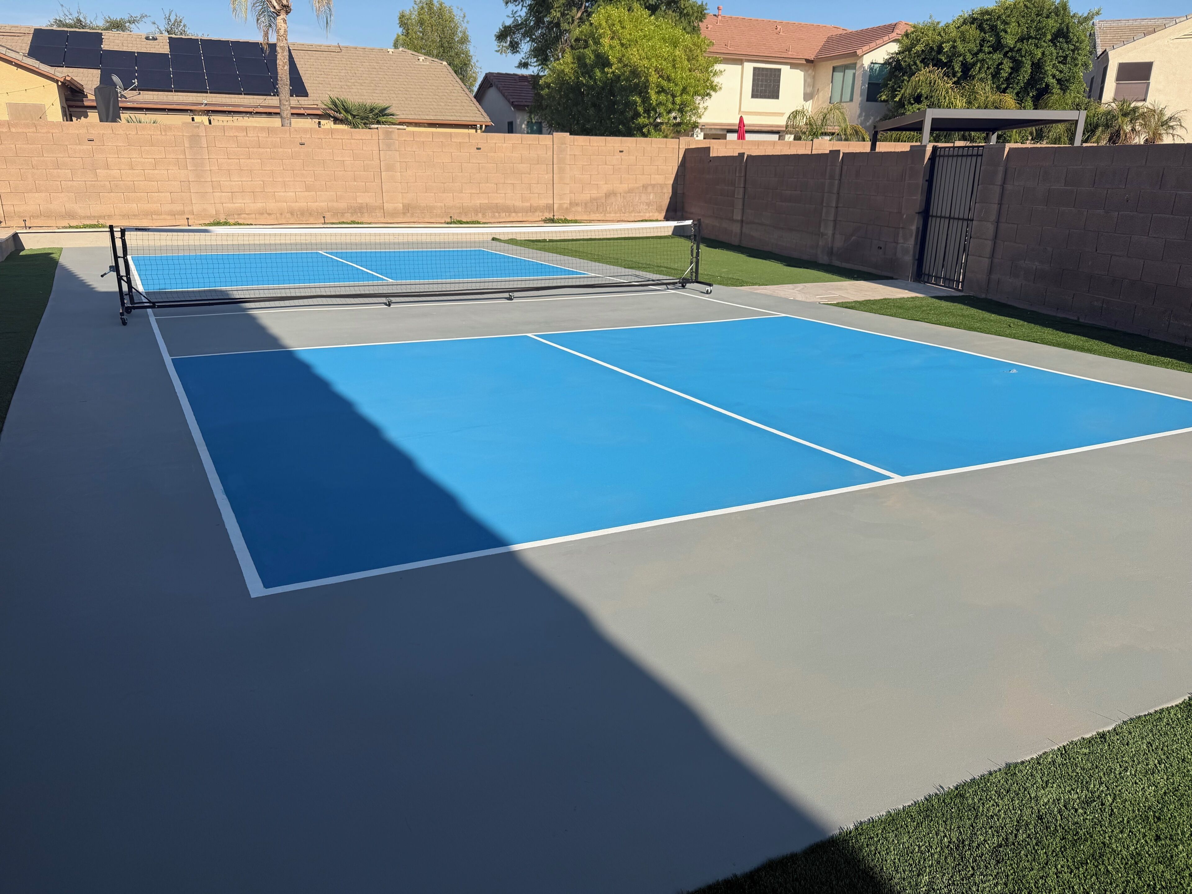 An outdoor tennis court with a net, surrounded by a brick wall and a fence.
