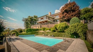 A modern house with a swimming pool, surrounded by well-maintained gardens and trees.