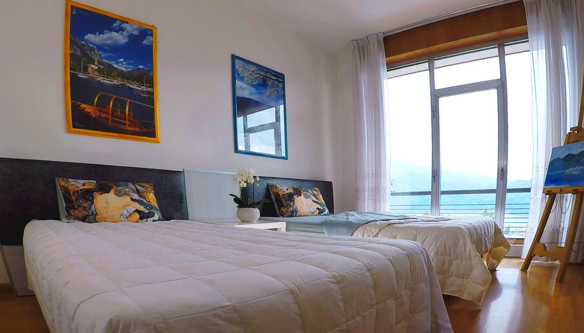 A hotel room with two beds, a large window with a view of the sea, and artwork on the walls.