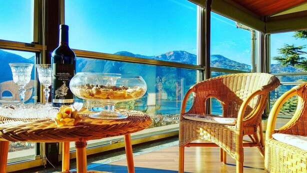 A balcony with wicker furniture, a glass table with a dessert, and a bottle of wine.