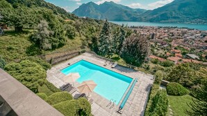 A rectangular swimming pool with a clear blue water, surrounded by a stone deck and equipped with lounge chairs and umbrellas.