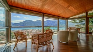 A spacious room with large windows offering a panoramic view of a coastal city and mountains.