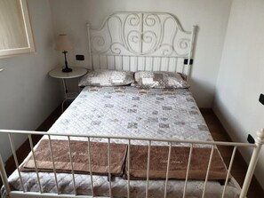 Een bed met een geborduurde sprei, twee kussens en een nachtkastje met een lamp.