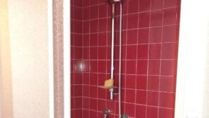 Doccia con piastrelle rosse, soffione a mano e spazzola esfoliante.