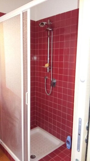 Een douche met rode tegels, een handdouche en een handscrubber.