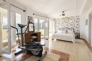 Camera da letto con un letto, attrezzature per l'esercizio fisico, una scrivania e ampie finestre.