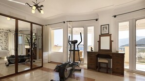 Une pièce spacieuse dotée d’un grand miroir, d’appareils de musculation, d’un bureau et offrant une vue sur l’extérieur.