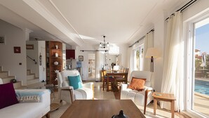 Un salon spacieux avec une table basse en bois, des canapés blancs et un coin repas comprenant une table et des chaises.