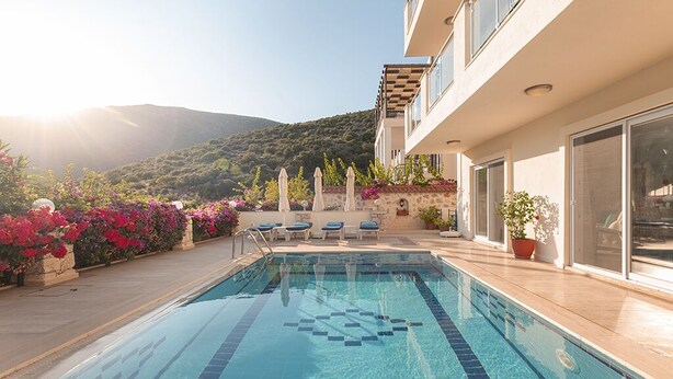 Une piscine entourée de chaises longues et de plantes en pot, le tout adossé à un bâtiment doté de grandes fenêtres et offrant une vue sur la montagne.