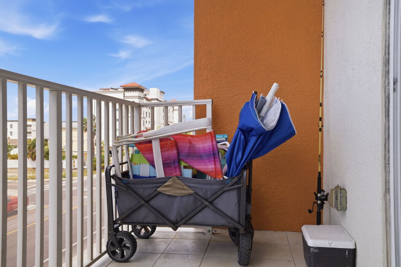 A balcony with a luggage cart, a blue umbrella, and a trash bin.