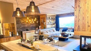 A modern living room with a wooden ceiling, a large wooden table, a sofa, and a television. - Chalet Angel - magnifique vue sur le lac (Les Angles)