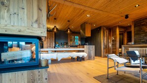 A wooden interior with a central seating area, a kitchen with modern appliances, and a fireplace. - Chalet Angel - magnifique vue sur le lac (Les Angles)