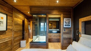 A wooden cabin interior with a large bed, a bathroom with a glass shower enclosure, and framed artwork on the walls. - Chalet Angel - magnifique vue sur le lac (Les Angles)