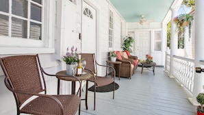 A covered porch with wicker furniture, a ceiling fan, and hanging plants. - Where Tranquility Blooms | Blossoms on Cannon (Charleston)