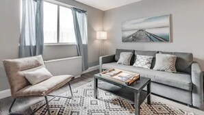 Uma sala de estar com sofá, poltrona, mesa de centro e um quadro na parede.