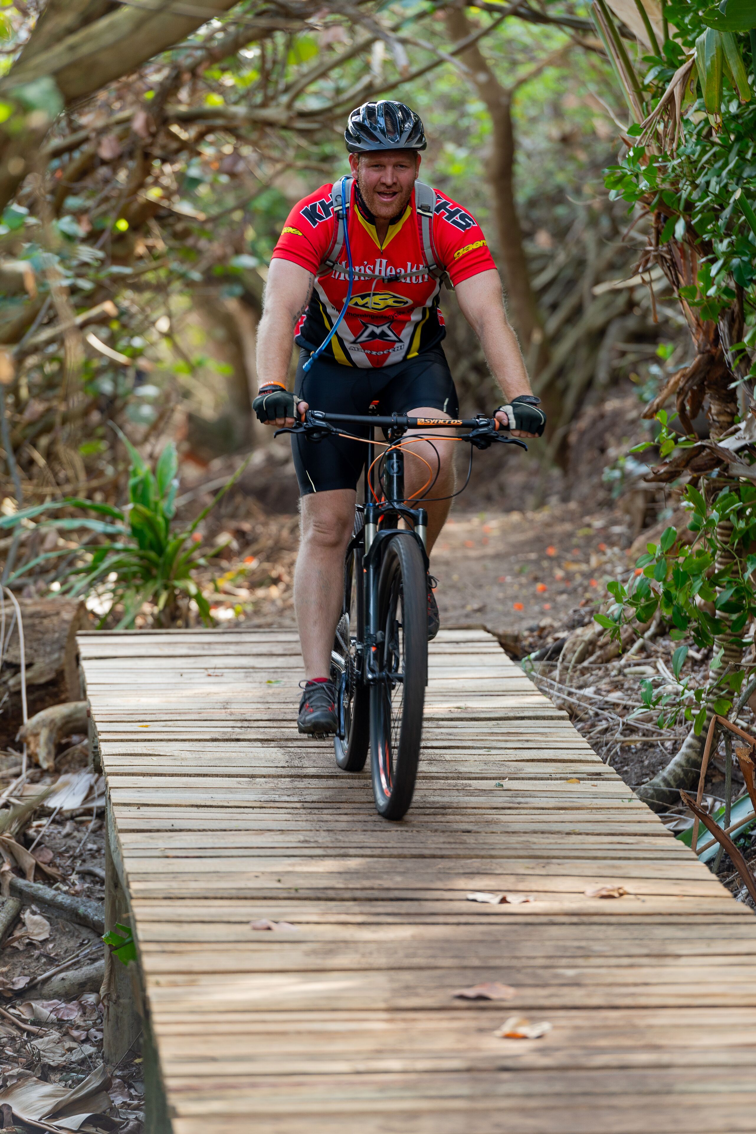 A person riding a bicycle on a wooden boardwalk surrounded by greenery.
