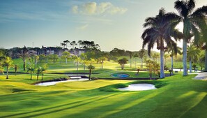 A golf course with sand bunkers, palm trees, and a water hazard.