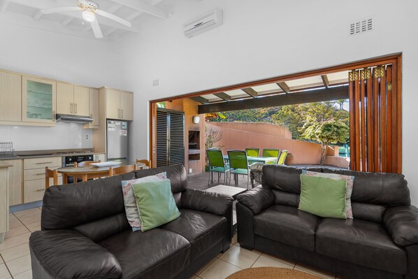 A modern kitchen with a built-in stove, a dining area with a table and chairs, and a living area with two leather sofas and a coffee table.