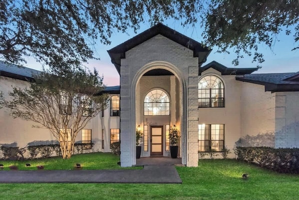 A two-story house with a prominent arched entrance, large windows, and a well-maintained lawn.