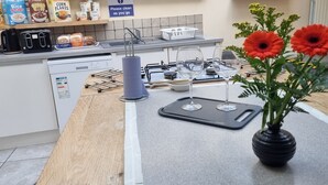 Ett kök med en diskho, en spis och diverse köksmaskiner. På köksbänken står det flingpaket och i en vas finns blommor.