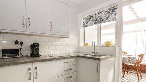 A modern kitchen with white cabinets, a granite countertop, a coffee maker, and a window with a floral curtain. - Sally's Berth (Scarborough)