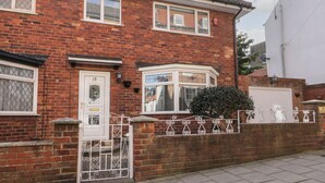 A two-story brick house with a white front door, a bay window, and a small garden. - Sally's Berth (Scarborough)