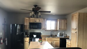 A kitchen with wooden cabinets, a black refrigerator, a microwave, a stove, and a ceiling fan. - Shedhorn Cabin #2 of 3 - 1 BEDR & Full RV Hookups (White Sulphur Springs)