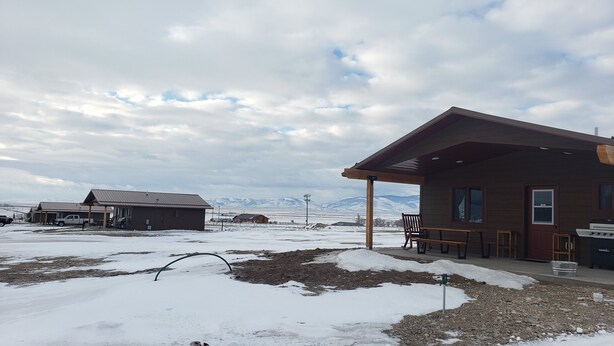 A rustic cabin with a patio, a truck, and a snowy landscape with mountains in the background. - Shedhorn Cabin #2 of 3 - 1 BEDR & Full RV Hookups (White Sulphur Springs)