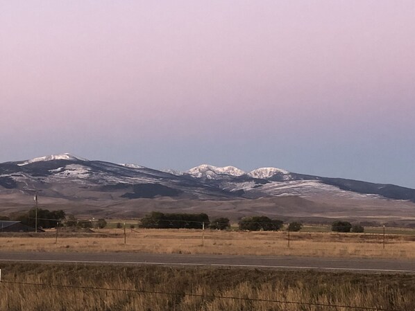 A mountain range with snow-capped peaks, a road in the foreground, and a flat landscape with sparse vegetation.