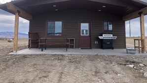 A rustic cabin with a covered porch, a door, and a grill. - Shedhorn Cabin #2 of 3 - 1 BEDR & Full RV Hookups (White Sulphur Springs)