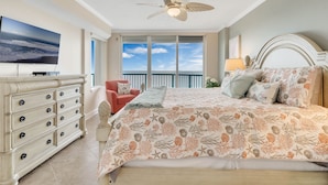 A bedroom with a large bed, a ceiling fan, a TV, a dresser, and a balcony with a view. - Oceanfront Penthouse ~ Professionally Designed (Daytona Beach Shore)